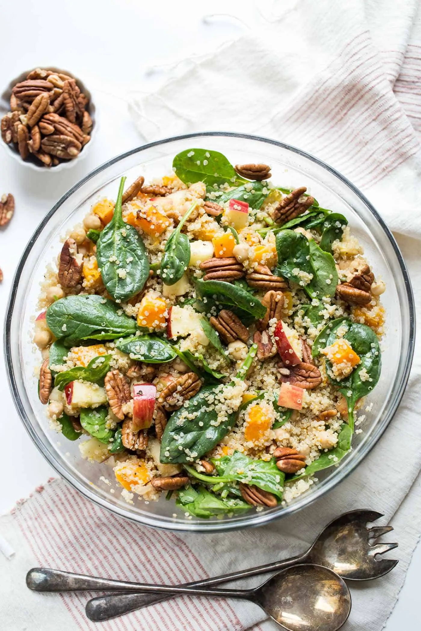 This simple butternut squash quinoa salad combines roasted squash, crispy apples, pecans and spinach for a hearty meal-sized salad. Overhead view of butternut squash quinoa salad in glass bowl