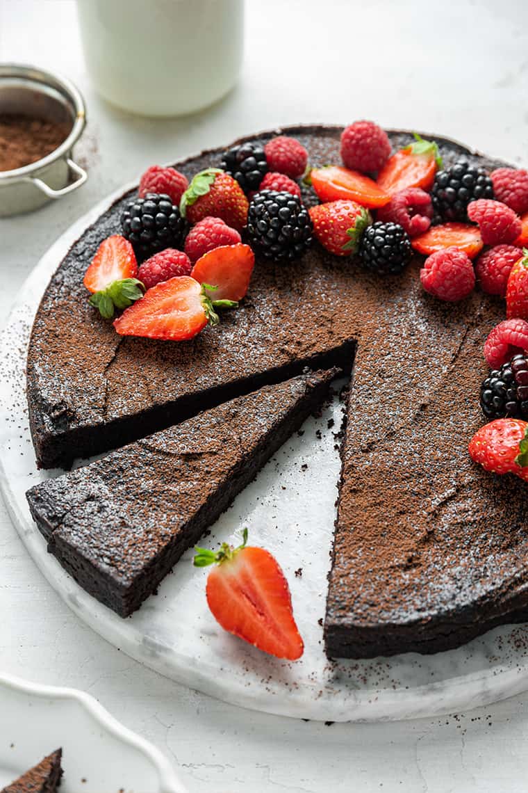 A chocolate cake with a slice removed, and one slice cut out, topped with strawberries, blackberries, and raspberries