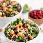 Two bowls of kale pomegranate salad next to a smaller bowl of pomegranate seeds.