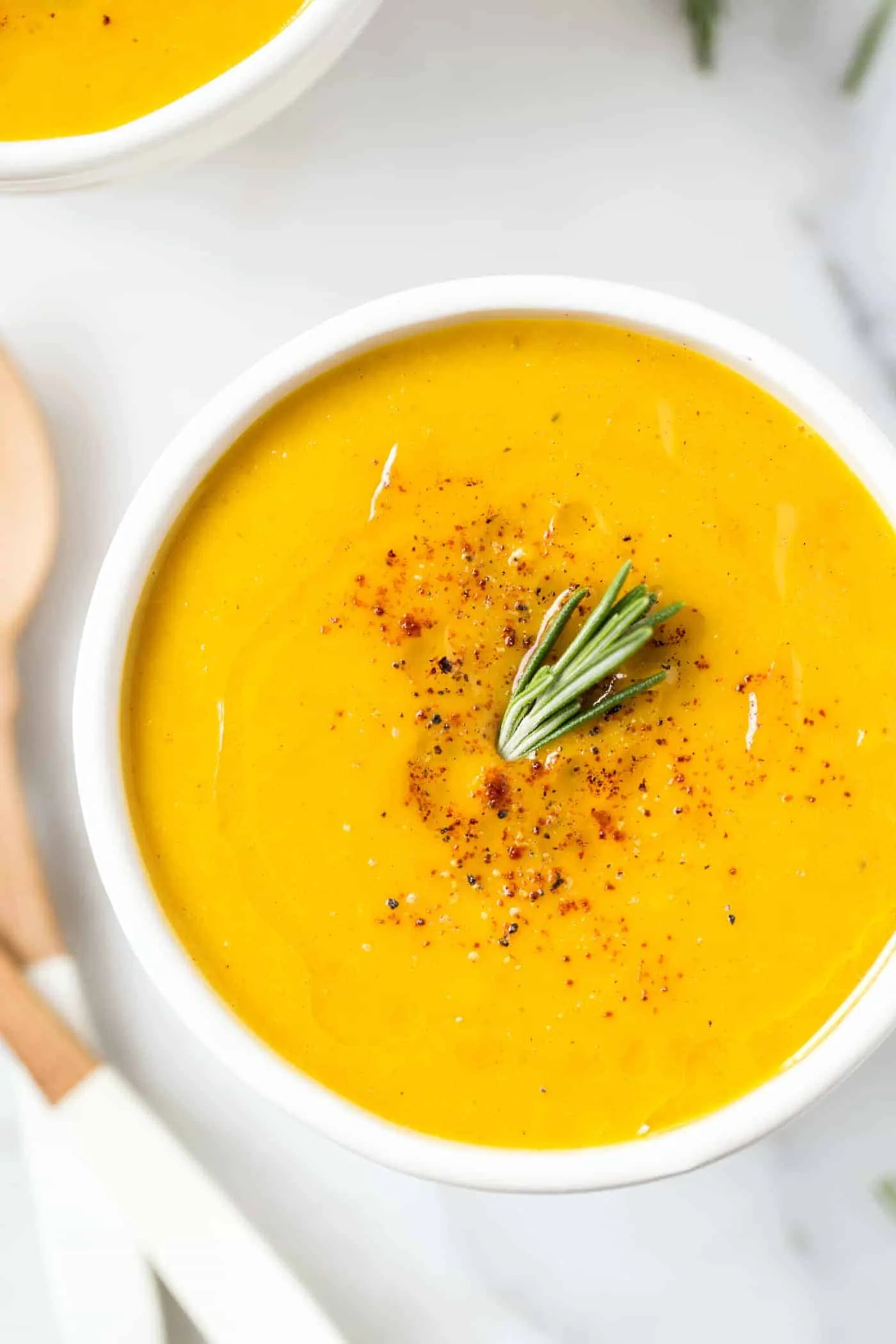 A bowl of squash soup topped with olive oil, black pepper, and fresh rosemary
