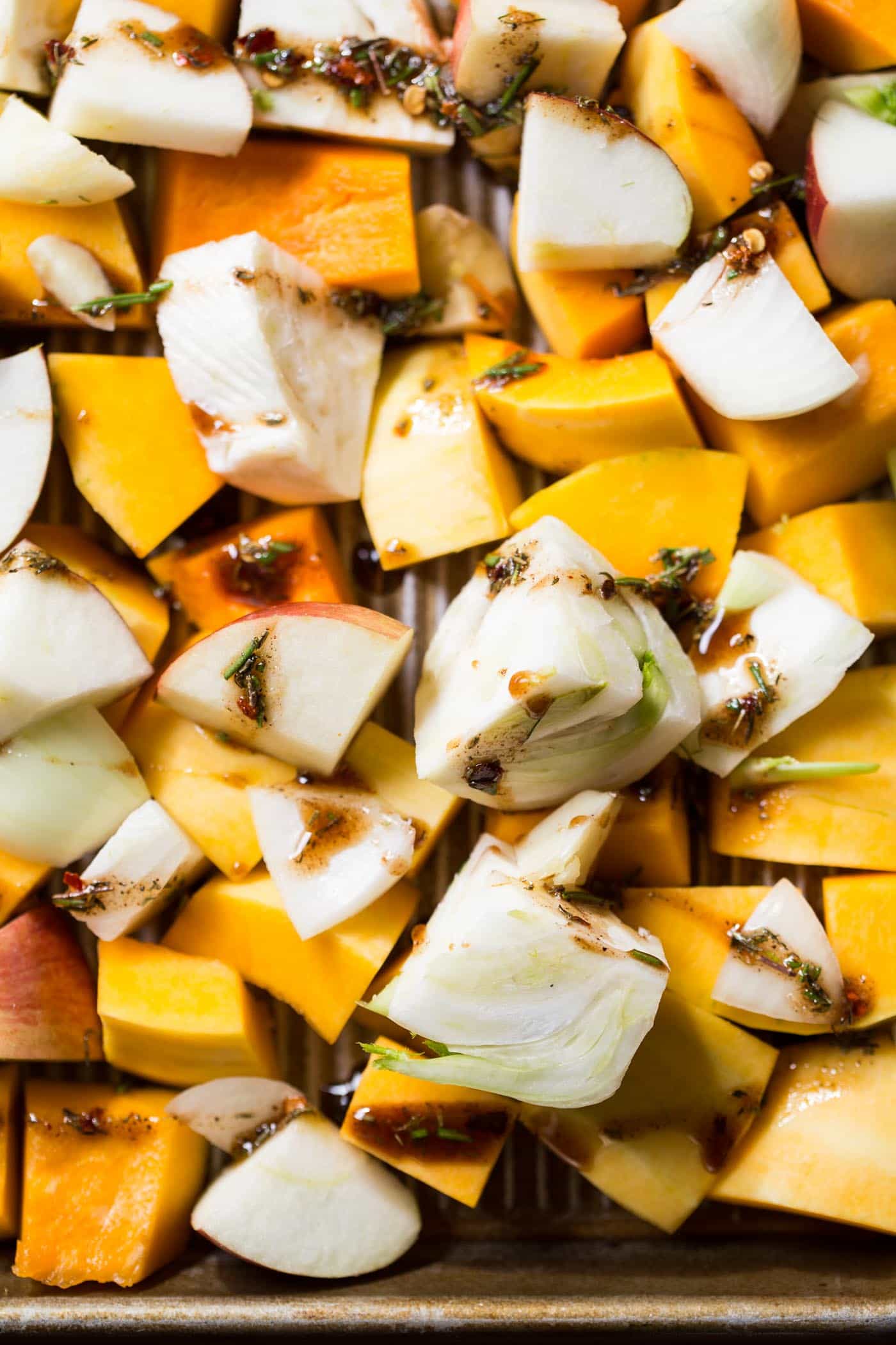 Raw cubed apples, squash, fennel, and onions, coated in herbs, spices, and oil
