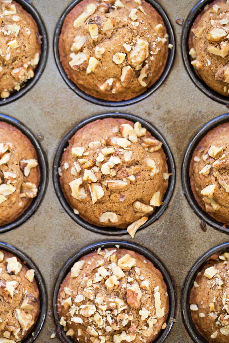 Overhead view of a muffin tin full of banana muffins topped with walnuts.