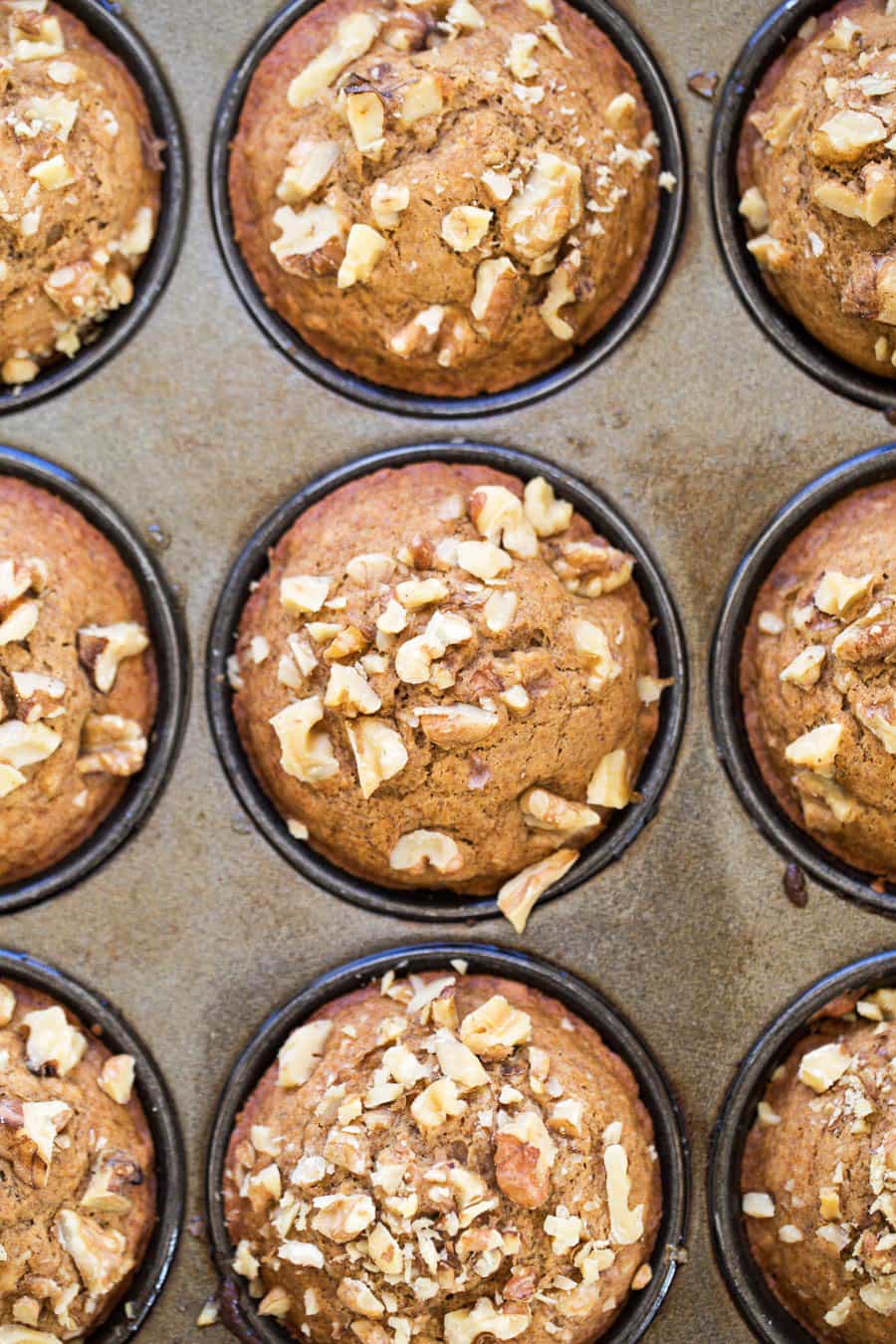 Overhead view of a muffin tin full of banana muffins topped with walnuts.