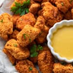 A serving tray of popcorn chicken garnished with parsley, with a bowl of dipping sauce