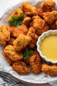 A serving tray of popcorn chicken garnished with parsley, with a bowl of dipping sauce