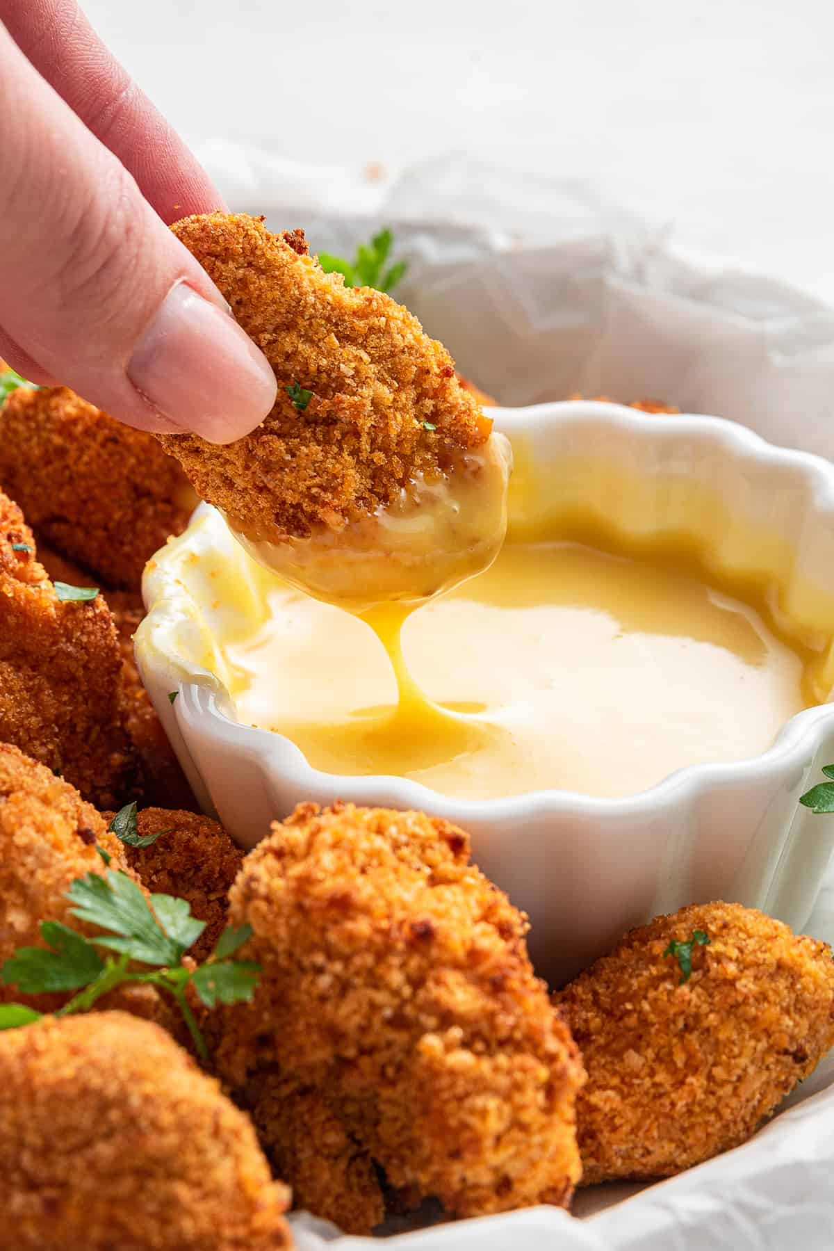 Close up of a hand pulling a piece of popcorn chicken out of a bowl of dipping sauce, with other pieces surrounding it