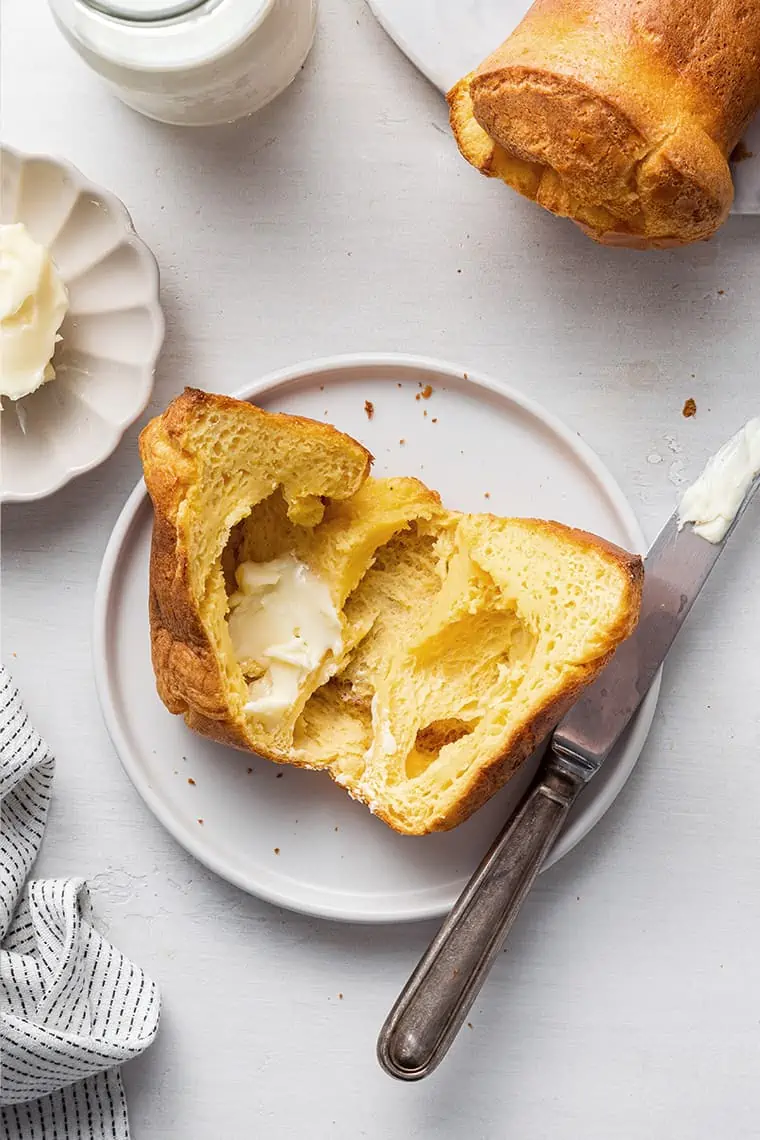 A gluten-free popover cut open, with a knob of butter on it, on a plate with a dirty butter knife