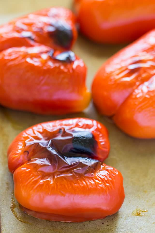 This easy and healthy roasted red pepper soup recipe has fresh tomatoes, quinoa, and lots of spices, and only takes an hour to make. Half of a red bell pepper that's black and charred on top, with three more surrounding it