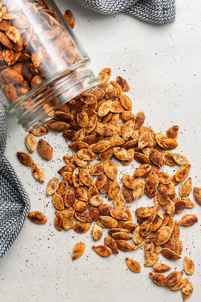Chili roasted pumpkin seeds being poured out of a jar