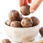 A hand picks up a peanut butter energy ball from a bowl of energy balls.