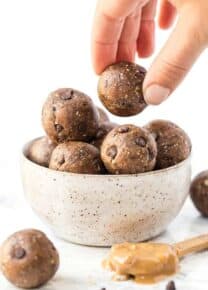 A hand picks up a peanut butter energy ball from a bowl of energy balls.
