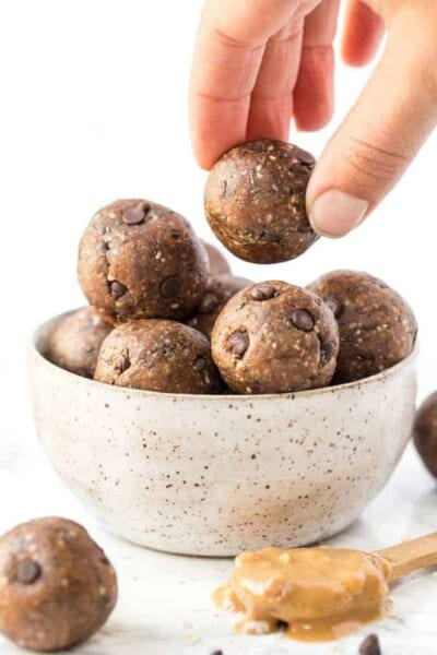 A hand picks up a peanut butter energy ball from a bowl of energy balls.