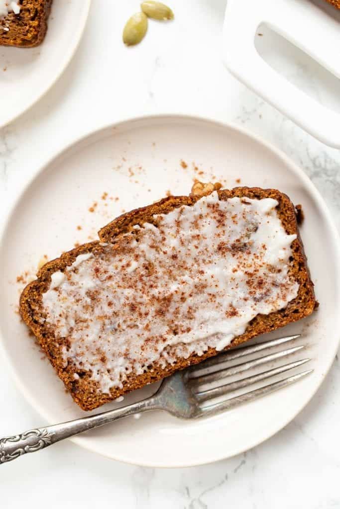 This soft, moist, flavorful gluten-free pumpkin bread recipe is a cozy fall breakfast! It's dairy-free, made with coconut flour in one bowl. Overhead view of a slice of gluten-free pumpkin bread spread with coconut butter on a plate with a fork.