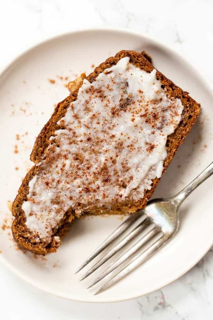 This soft, moist, flavorful gluten-free pumpkin bread recipe is a cozy fall breakfast! It's dairy-free, made with coconut flour in one bowl. Overhead view of a slice of gluten-free pumpkin bread spread with coconut butter on a plate, with a bite missing.