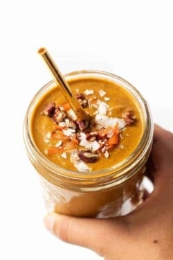 Hand holding carrot cake smoothie in glass.
