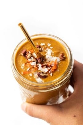 Hand holding carrot cake smoothie in glass.