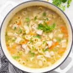 Overhead view of a dutch oven filled with chicken noodle soup, garnished with parsley