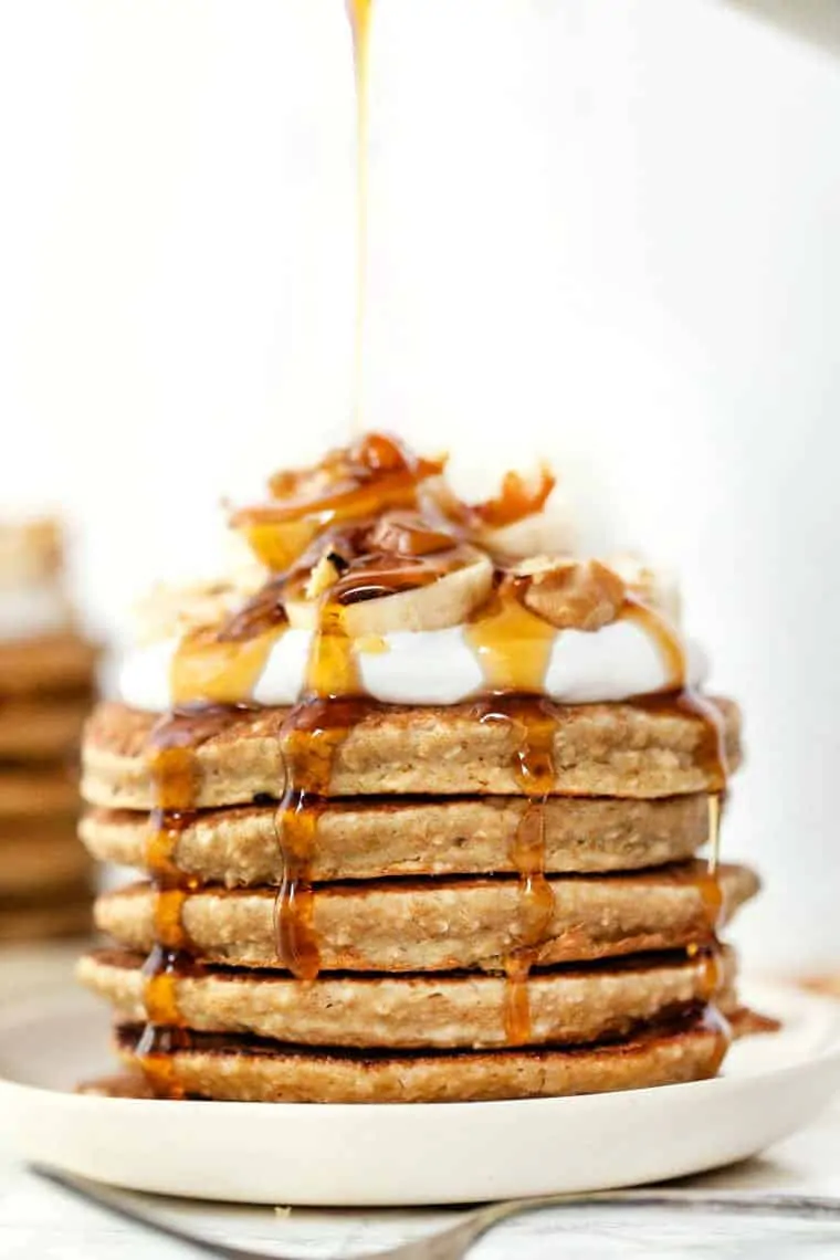 Side view of syrup being poured over stack of quinoa banana pancakes