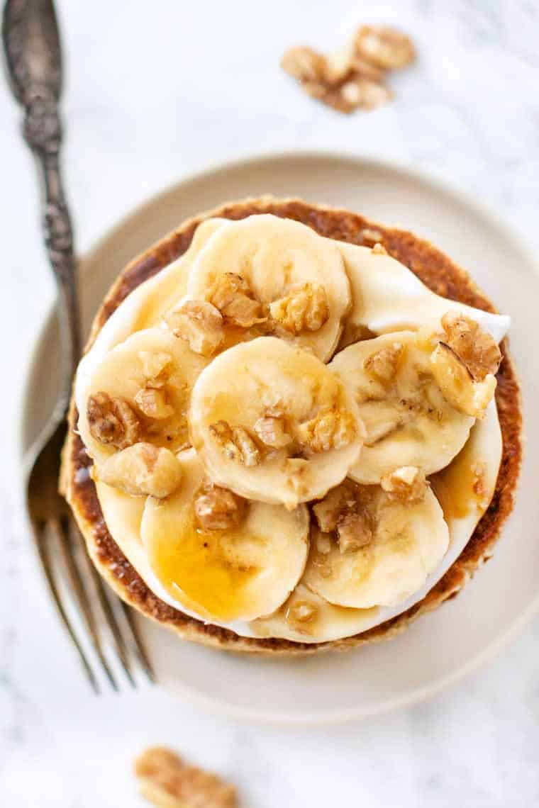 Overhead view of quinoa banana pancakes topped with walnuts, syrup, and bananas