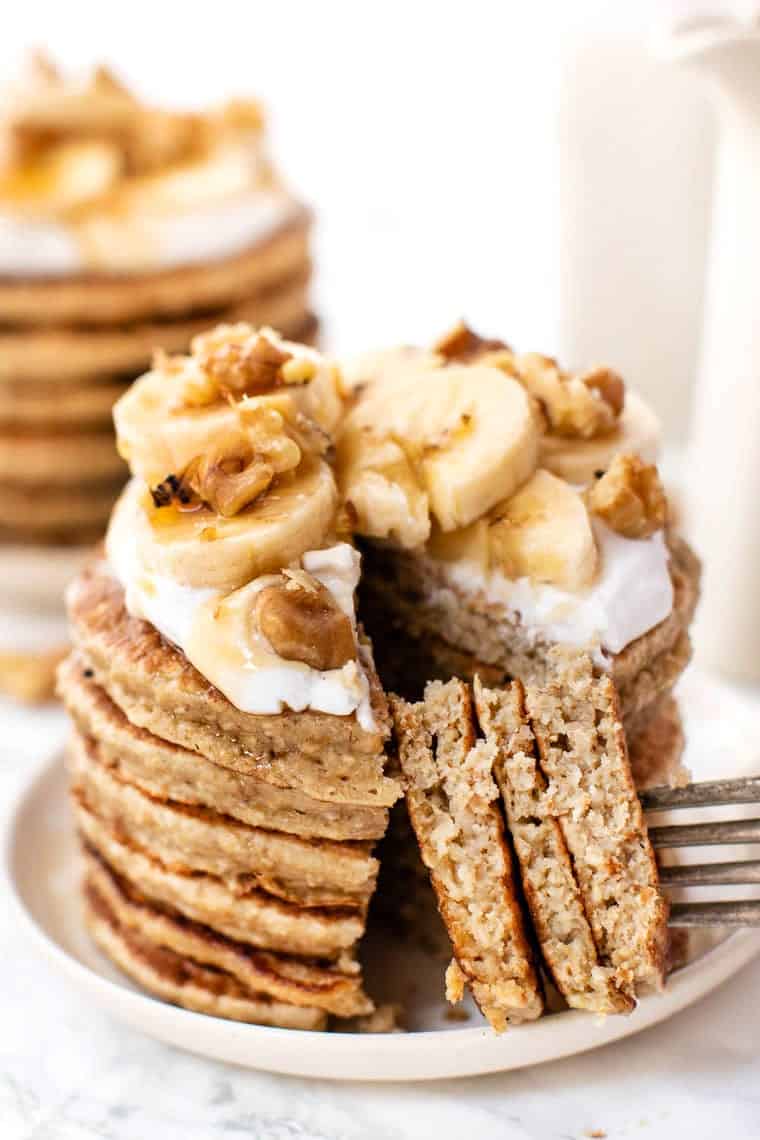 Quinoa banana pancakes stacked on plate, with fork removing bite