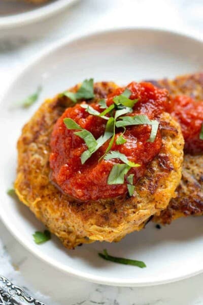 Close up of two spaghetti squash fritters topped with salsa on a white plate.