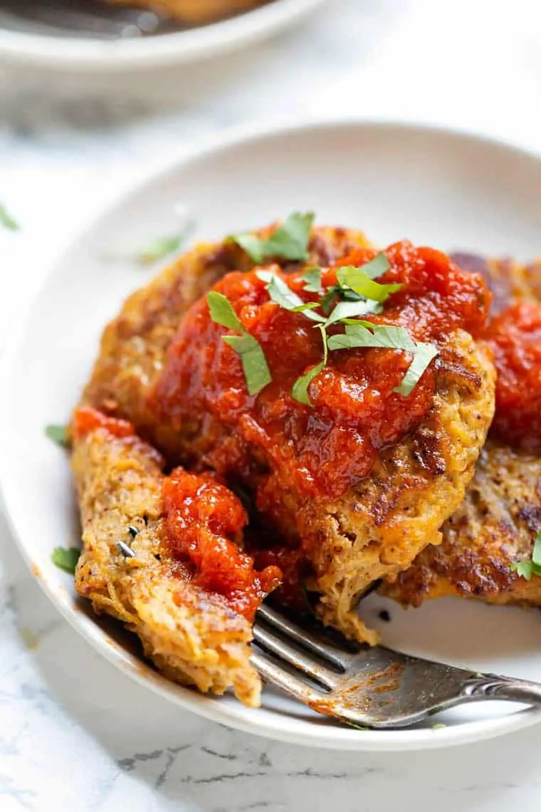 A fork cutting a salsa-covered squash patty in half on a white plate.