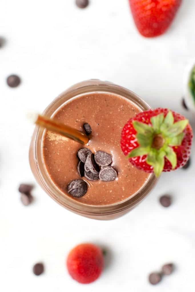 This chocolate strawberry smoothie is tastes like chocolate-covered strawberries! It's packed with frozen berries, cocoa, and hemp seeds. Overhead view of a chocolate strawberry smoothie in a glass jar garnished with chocolate chips and a fresh berry.