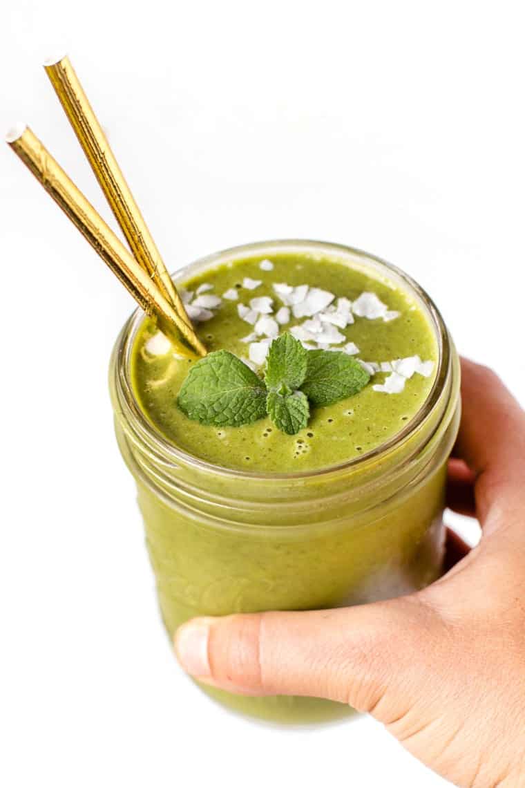 This minty cantaloupe melon smoothie is packed with protein and nutrients. Kale, melon and cucumber make for a vibrant, summery smoothie! Hand holding cantaloupe melon smoothie in jar
