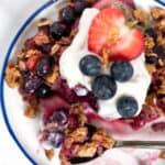 Overhead view of a serving of berry crumble on a plate topped with yogurt and fresh berries.