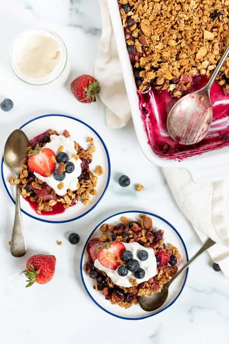 Overhead view of servings of berry crumble served on two plates, next to the rest of the crumble in a baking dish.