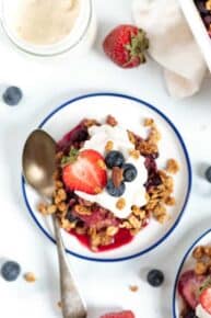 Overhead view of a serving of berry crumble on a plate topped with yogurt and fresh berries.