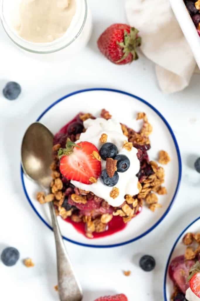 Overhead view of a serving of berry crumble on a plate topped with yogurt and fresh berries.