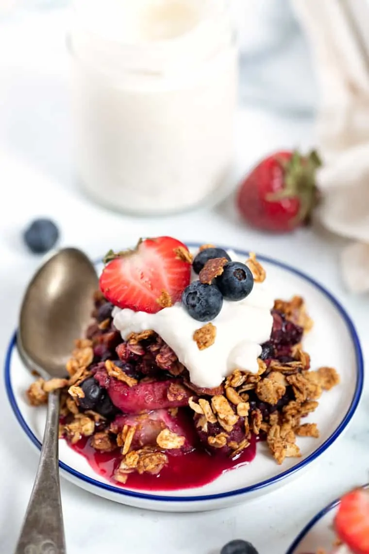 This quick and easy mixed berry crumble uses fresh or frozen berries, is vegan, gluten-free, and SO easy to make. The perfect summer dessert! A serving of mixed berry crumble on a plate topped with yogurt and fresh berries, with a spoon.