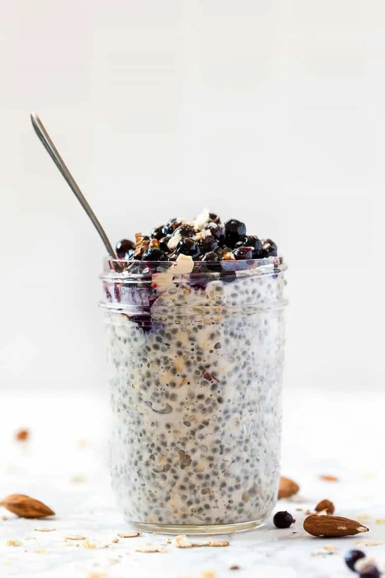 A jar of chia pudding topped with blueberries, with a spoon in it.