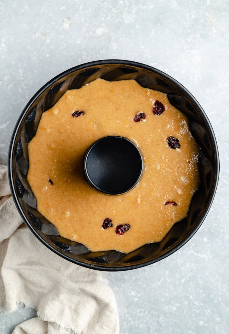 A bundt pan filled with cranberry orange coffee cake batter, with lots of dried cranberries in it.