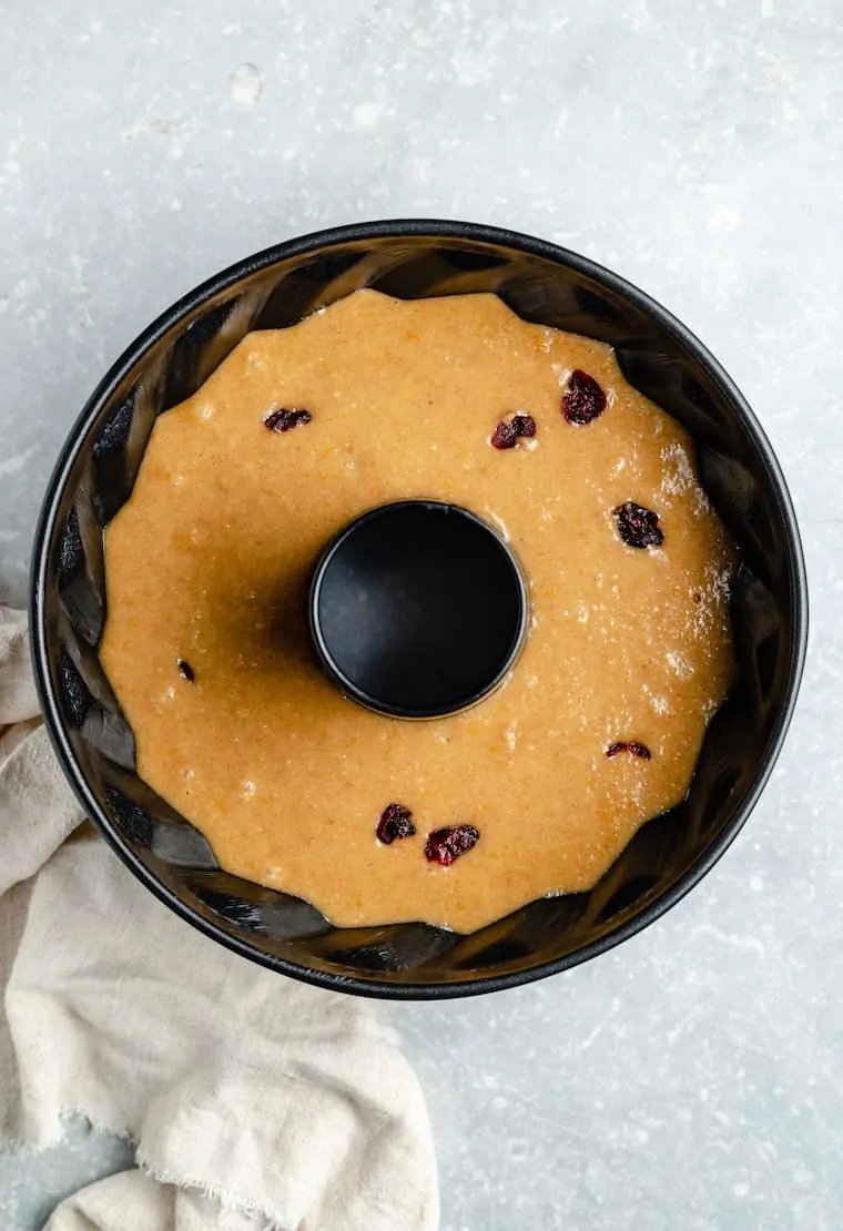 A bundt pan filled with cranberry orange coffee cake batter, with lots of dried cranberries in it.