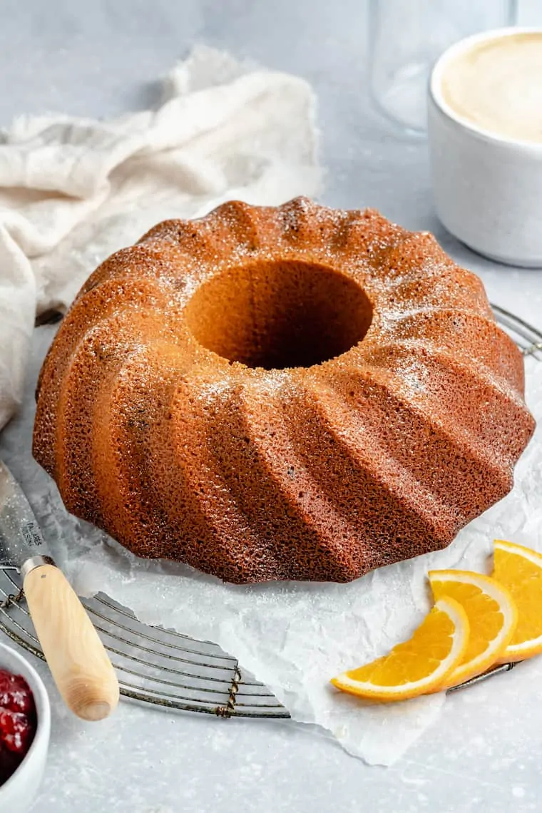 A round cranberry orange coffee cake on a wire rack, next to three orange slices.