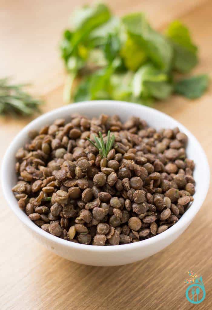 A bowl of brown lentils topped with a sprig of rosemary