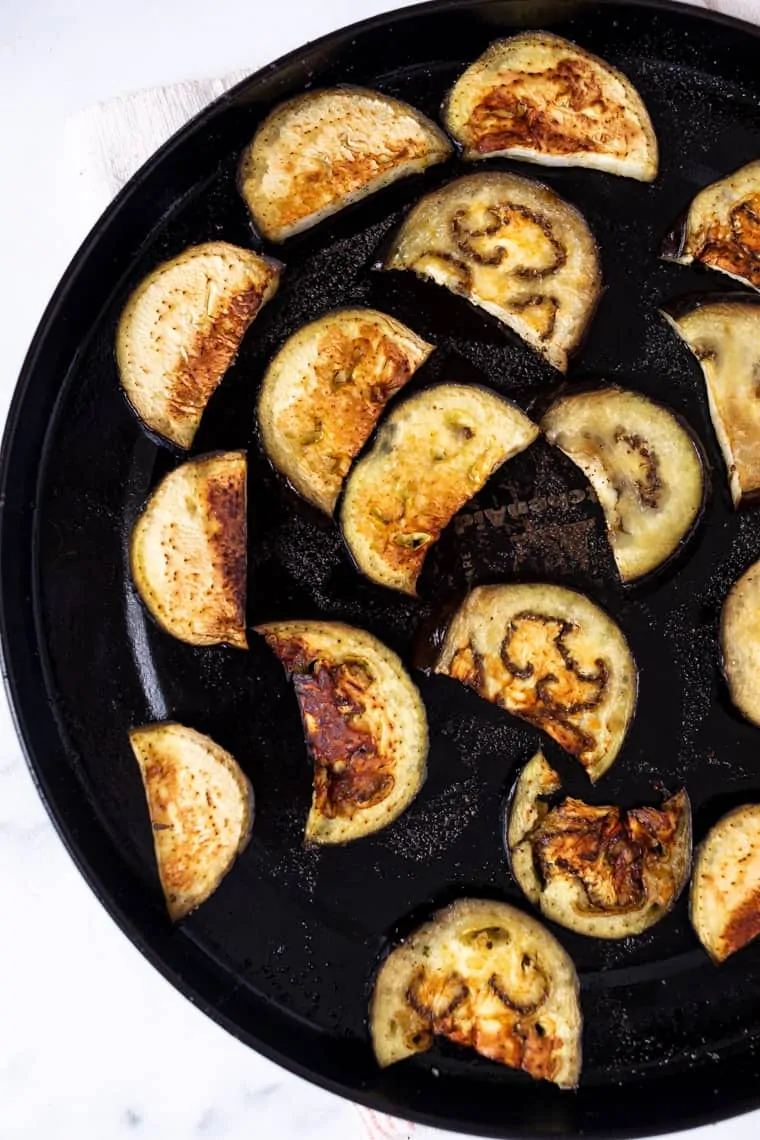 Overhead view of half moons of eggplant roasting in a dish