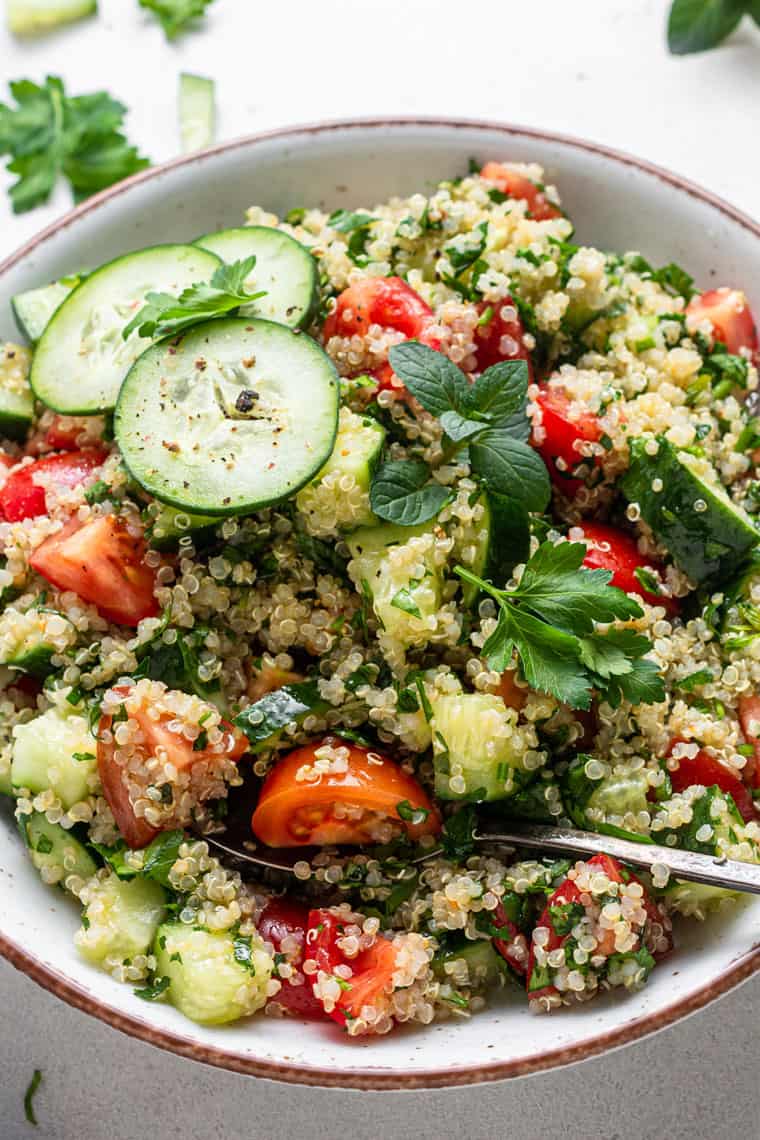 This healthy quinoa tabbouleh salad is light, refreshing, and flavorful. It's also quick and easy, requiring only a few simple ingredients! white bowl with quinoa tabbouleh salad with cucumbers and tomatoes