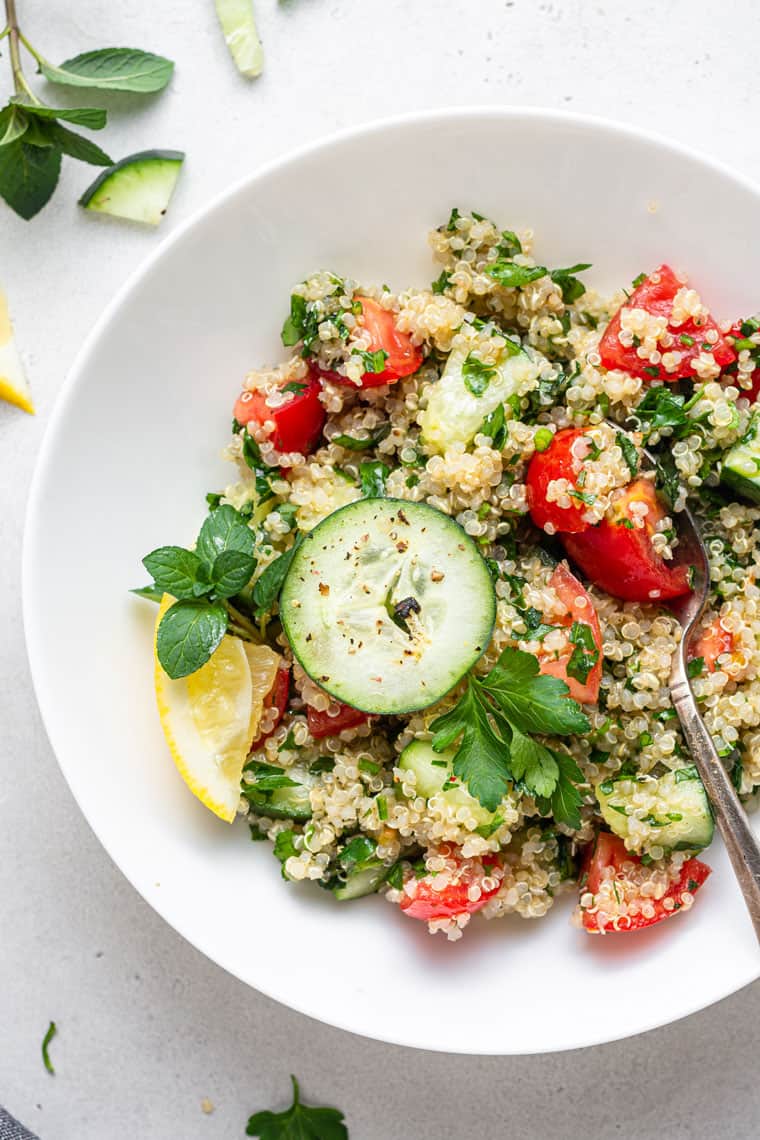 This healthy quinoa tabbouleh salad is light, refreshing, and flavorful. It's also quick and easy, requiring only a few simple ingredients! white bowl with quinoa tabbouleh recipe topped with sliced cucumber, cracked pepper and parsley