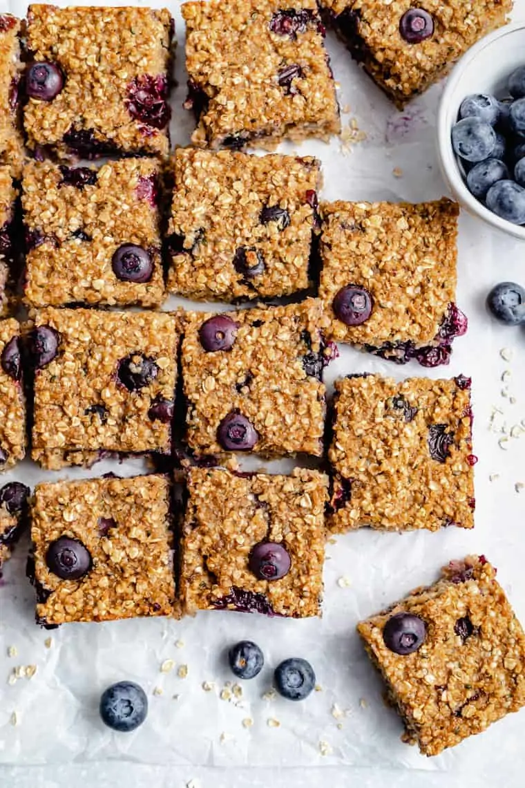 overhead of many blueberry breakfast bars on a white piece of parchment paper with fresh berries