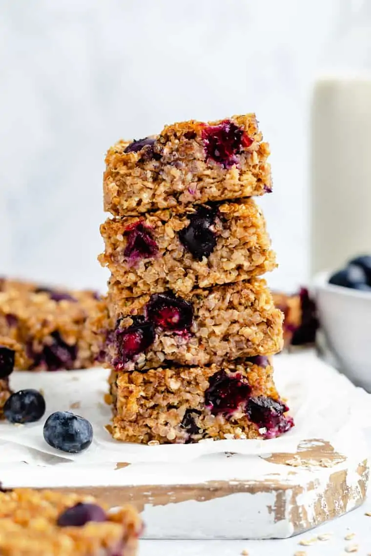 stack of blueberry quinoa breakfast bars on a cutting board with fresh blueberries