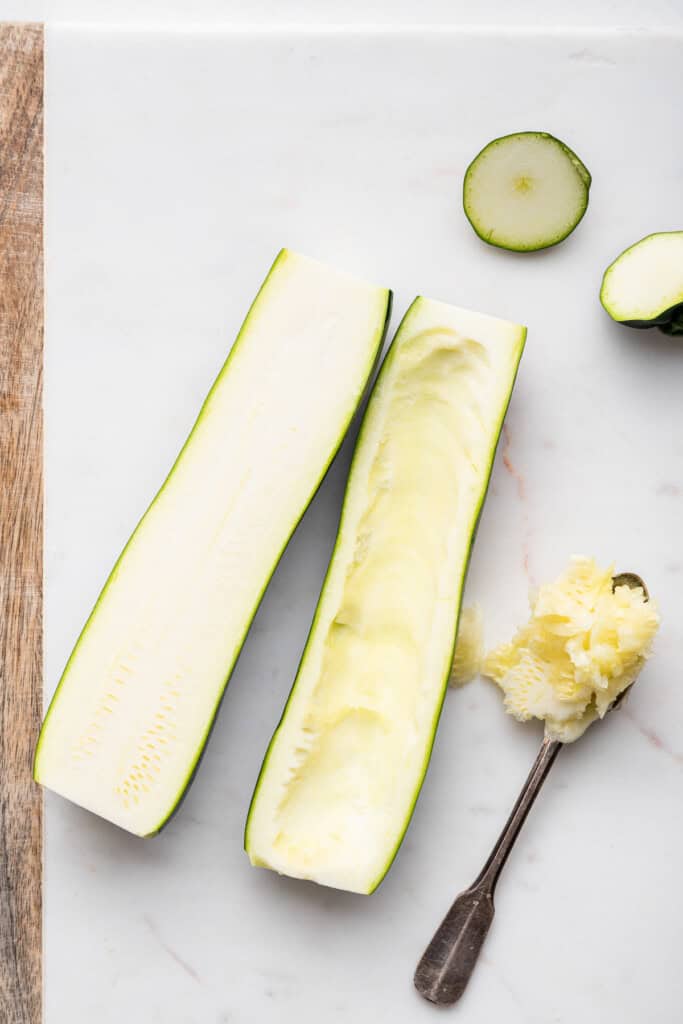 Overhead view of 2 zucchini halves on cutting board with seeds scooped out of one half