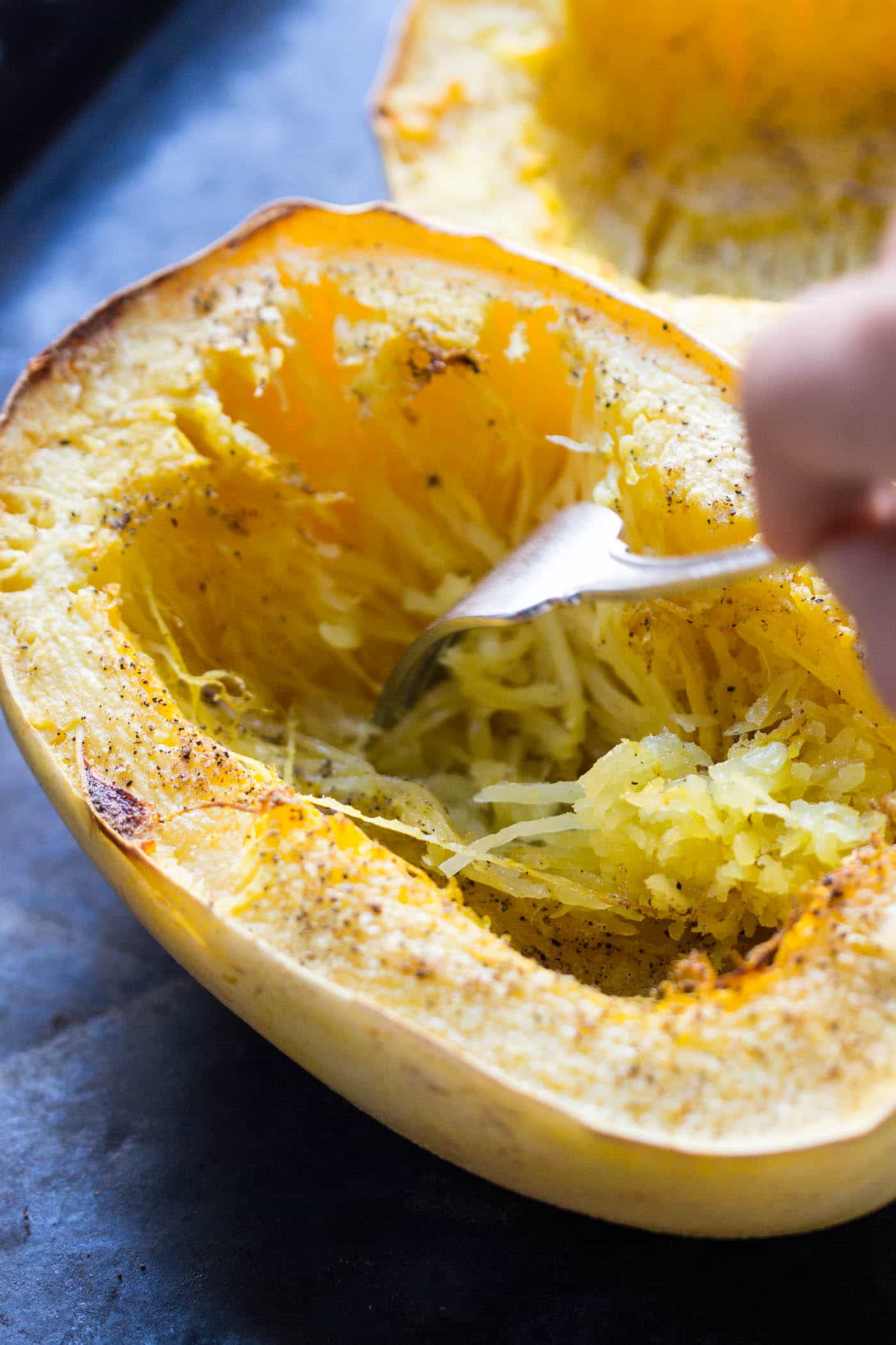 A hand uses a fork to hollow out one half of a cooked spaghetti squash.