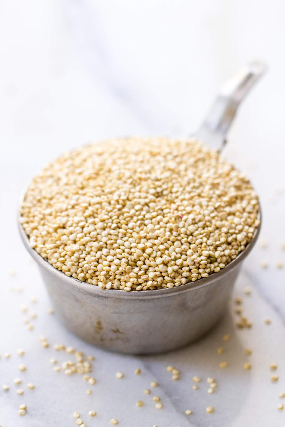 A measuring cup full of quinoa, surrounded by quinoa