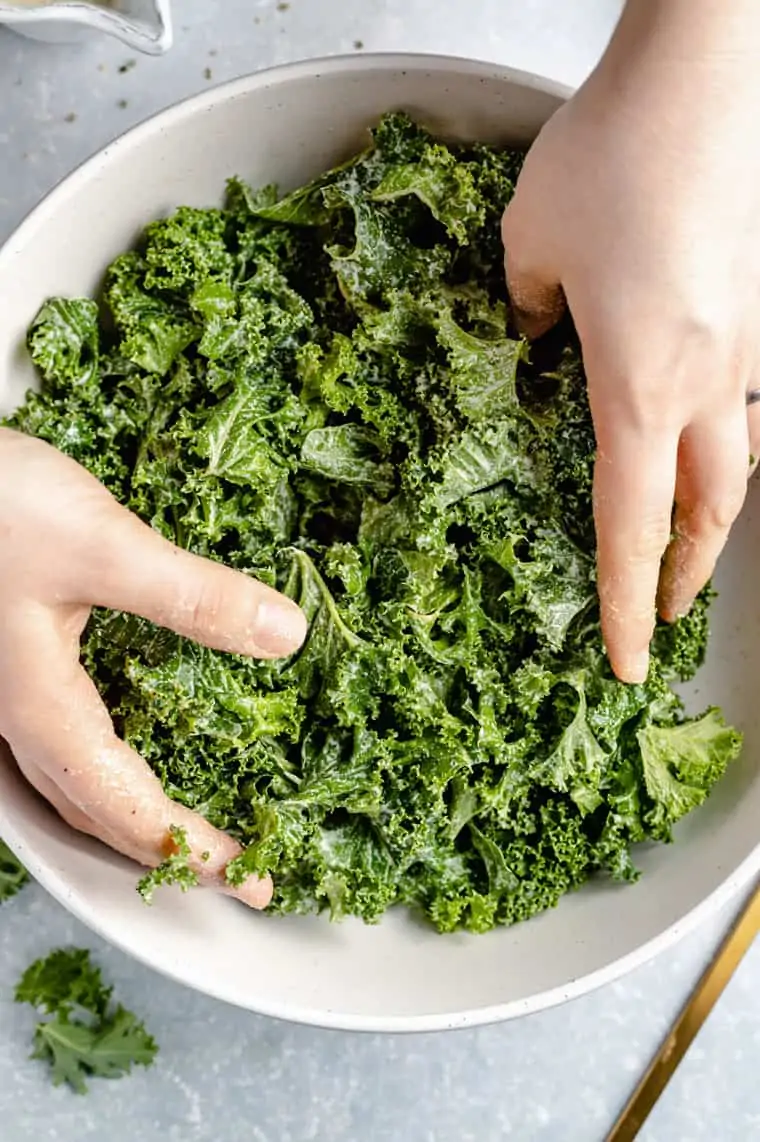 Overhead view of two hands massaging kale in a bowl