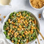 Overhead view of vegan Caesar kale salad in a white bowl topped with crispy chickpeas and tahini dressing.