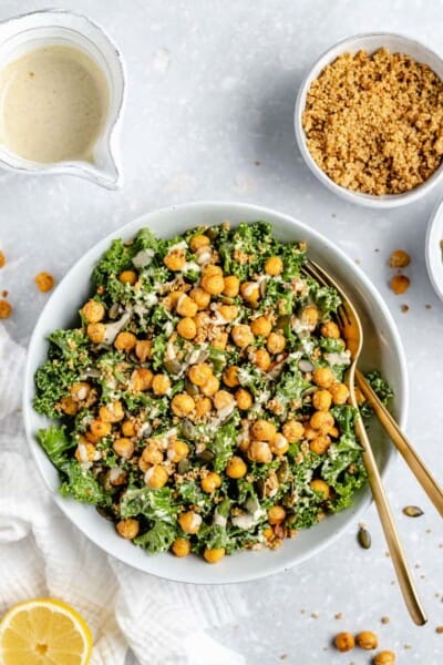 Overhead view of vegan Caesar kale salad in a white bowl topped with crispy chickpeas and tahini dressing.