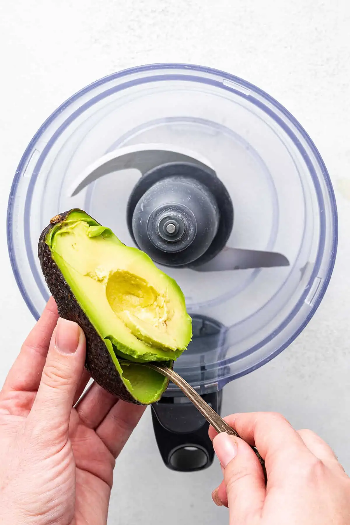 Scooping ripe avocado into a food processor.